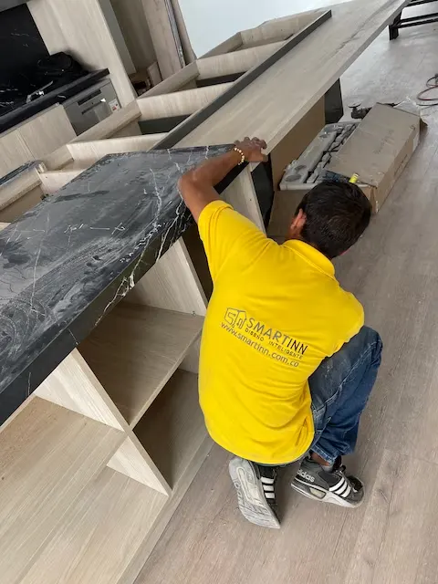Integrante de Smartinn con la camiseta de la empresa instalando un mesón de mármol sobre los muebles de una cocina