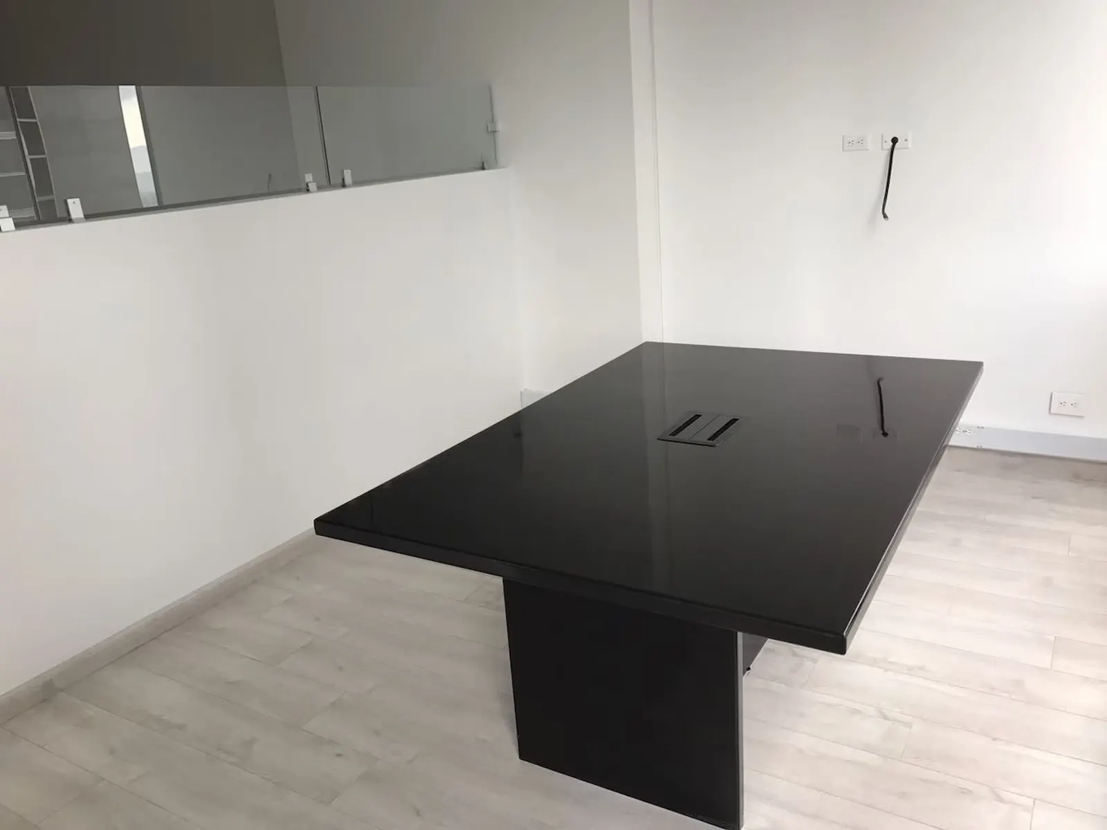 Mesa de reuniones negra en una oficina remodelada, con piso de madera clara y barandas de vidrio