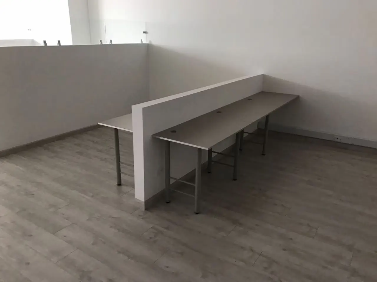 Puestos de trabajo con escritorios corridos y un tabique blanco en una oficina con piso gris
