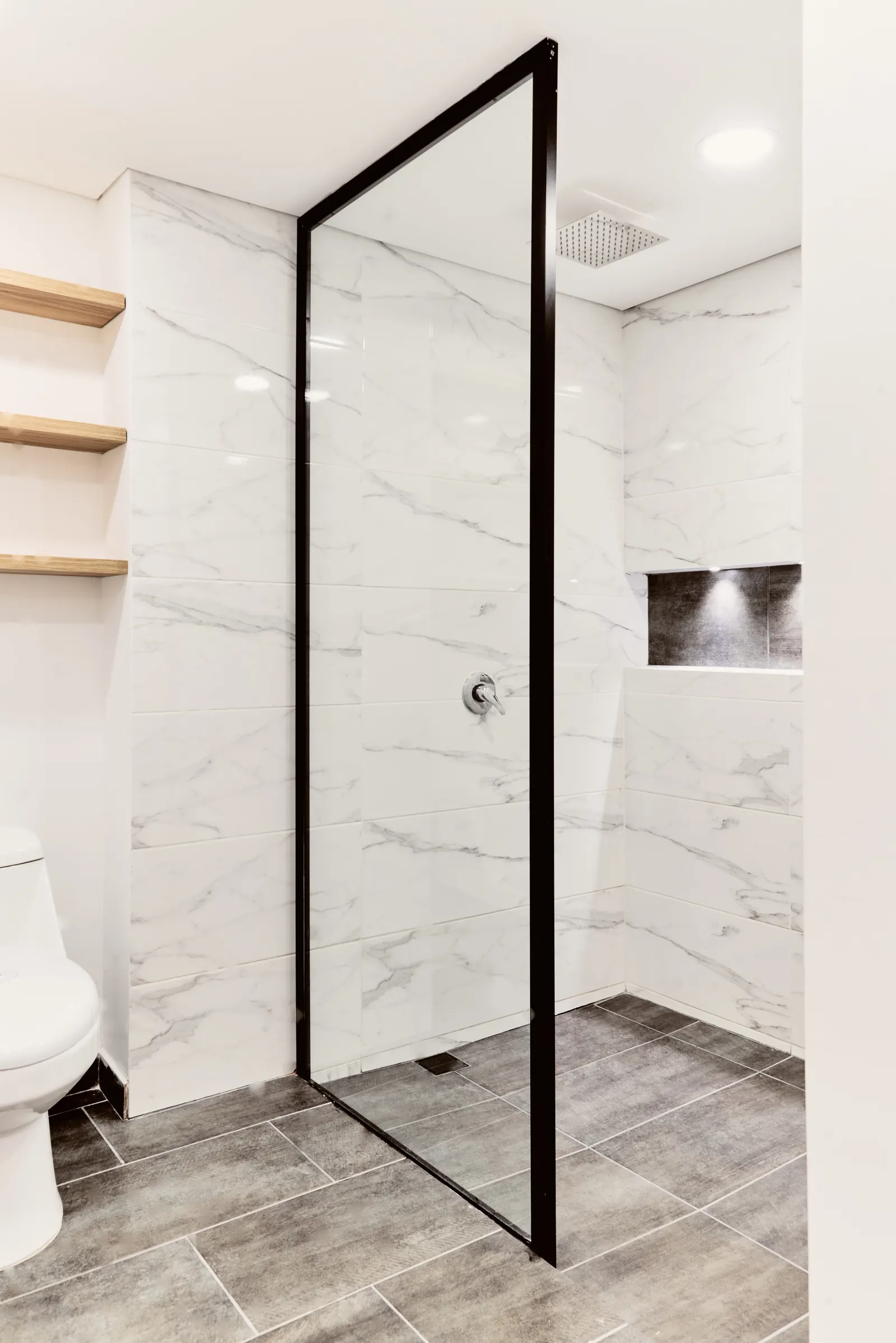 Ducha con porcelanato tipo mármol, división de vidrio con perfil negro y repisas de madera