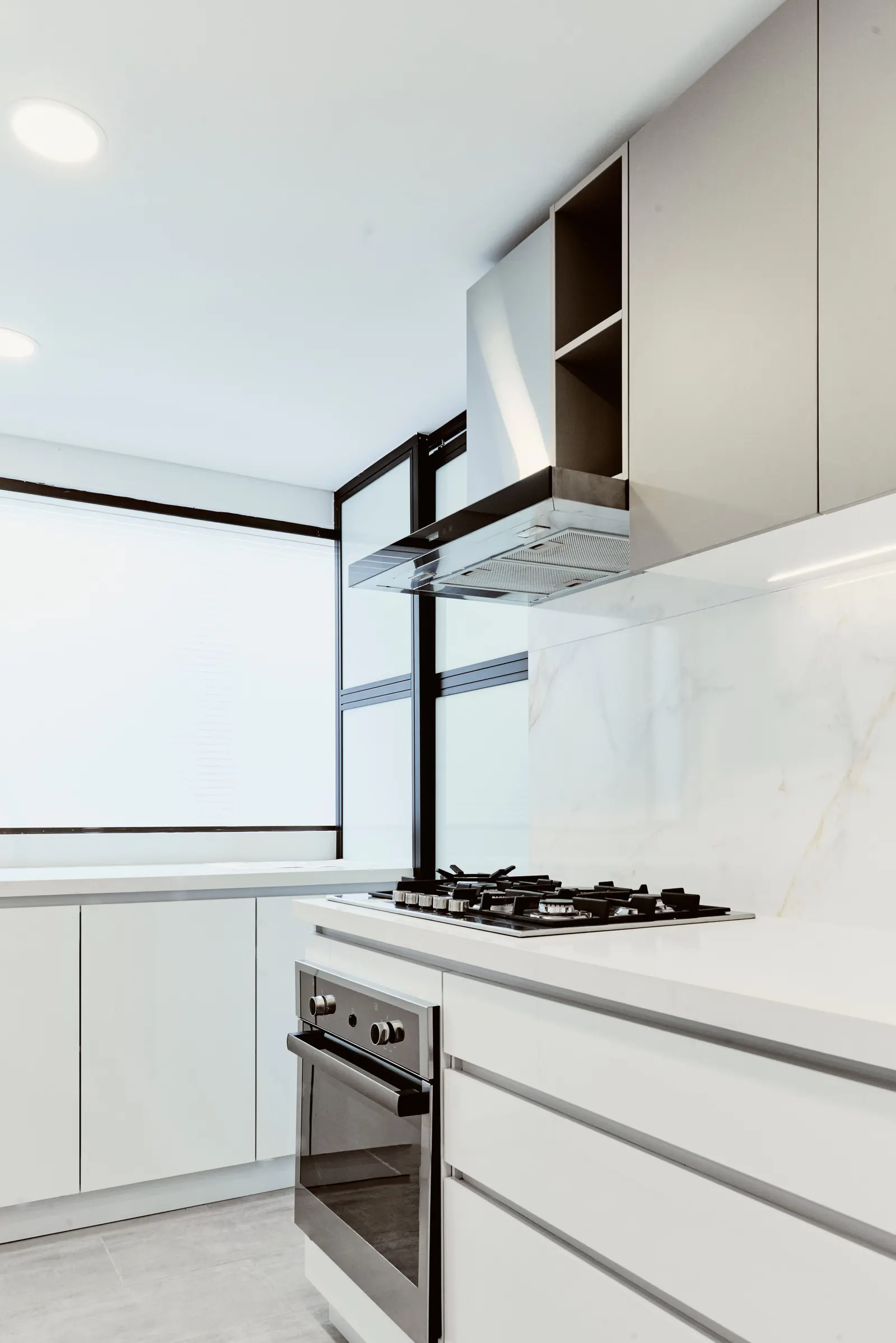 Estufa a gas con campana, horno empotrado y salpicadero claro con veta en una cocina blanca