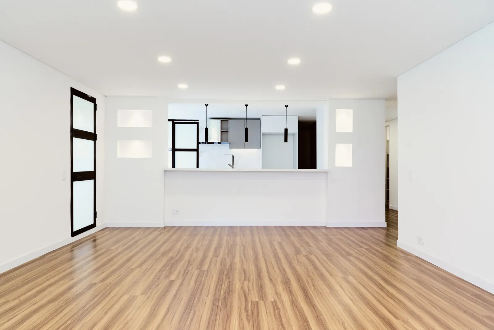 Sala amplia con piso de madera y cocina abierta con barra y lámparas colgantes en un apartamento remodelado en el Chicó