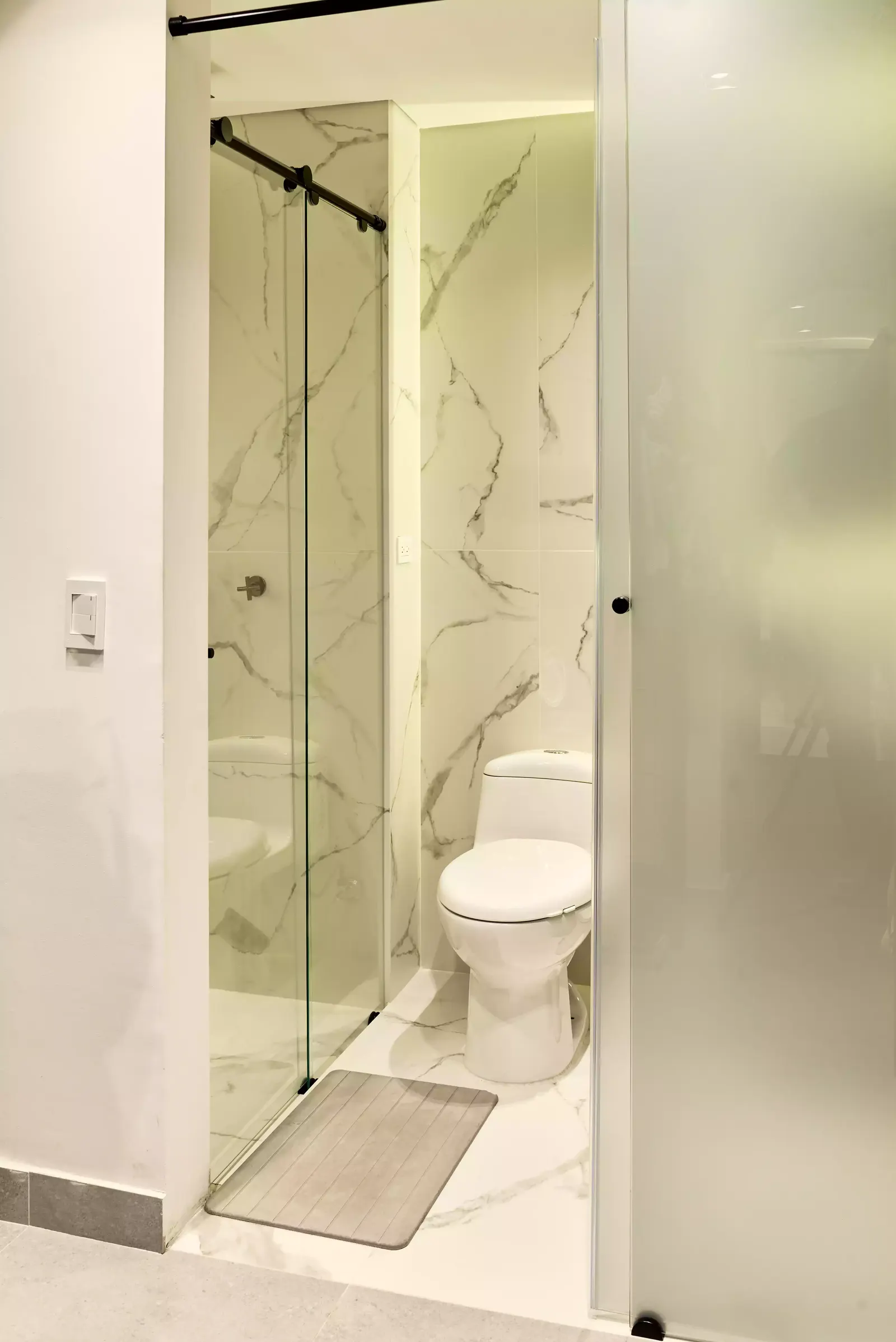 Baño con ducha en vidrio y revestimiento claro con veta