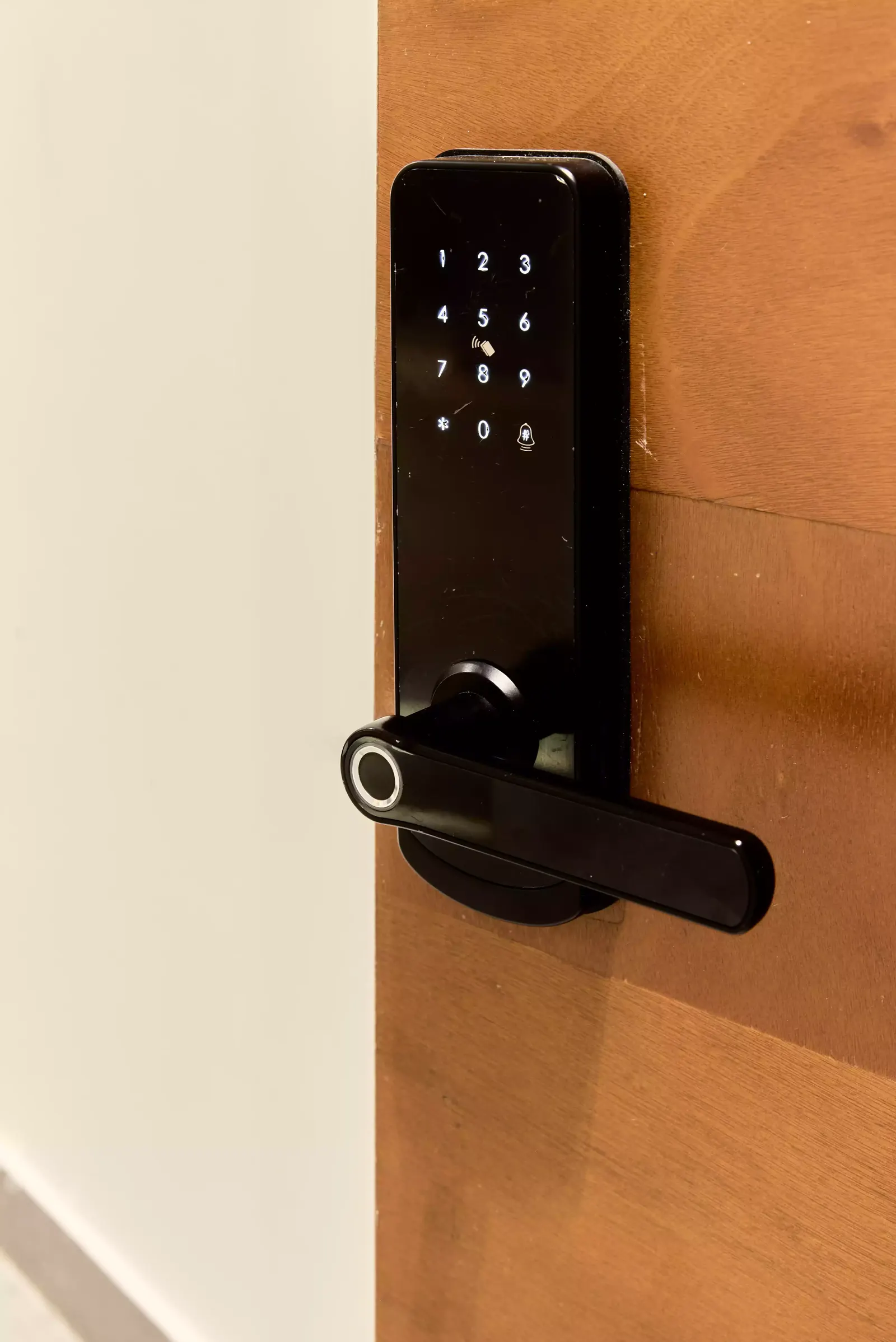 Cerradura inteligente negra con teclado numérico y lector de huella sobre una puerta de madera