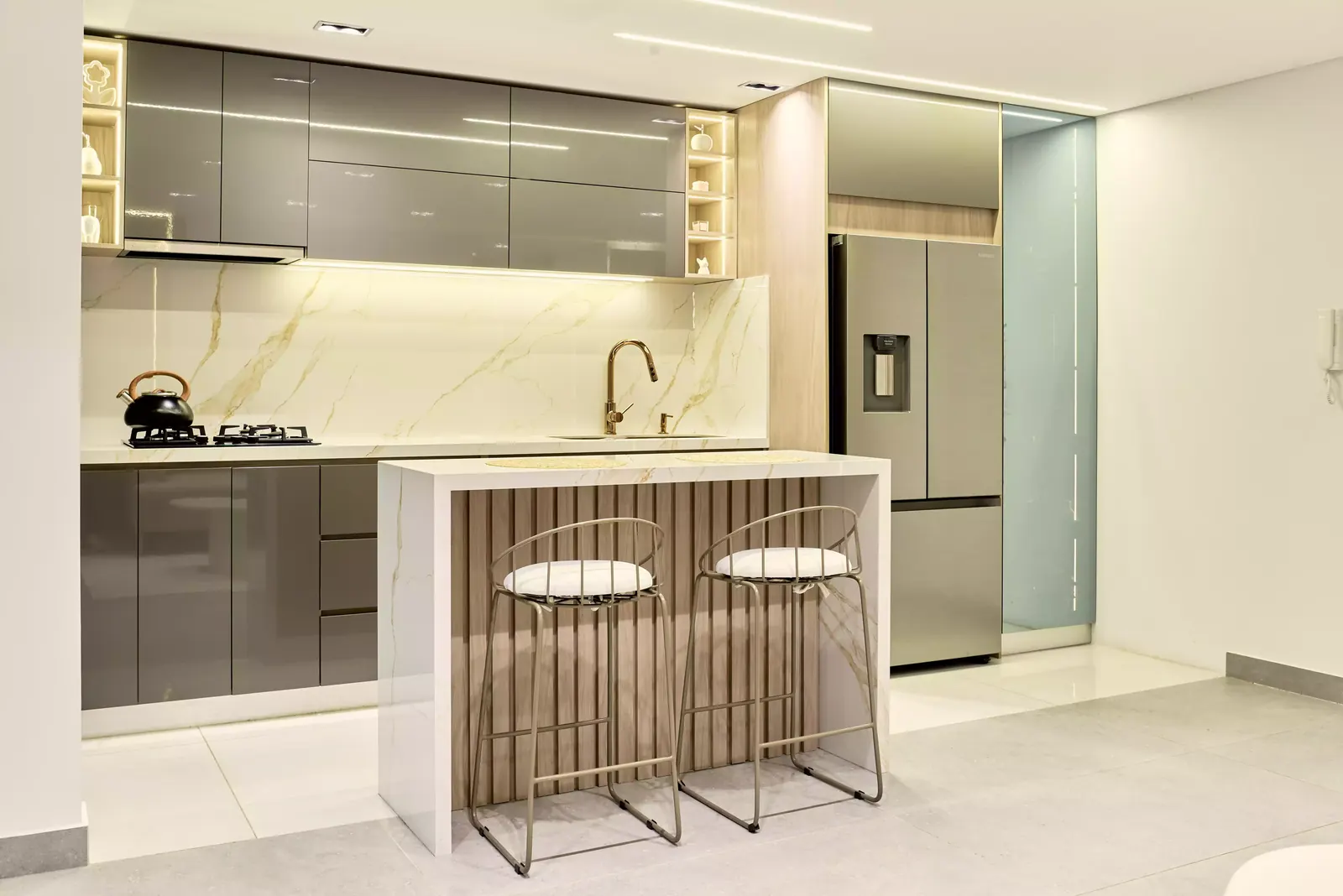 Cocina con isla, frentes de alto brillo e iluminación bajo las alacenas en un apartamento minimalista de tonos beige y blanco