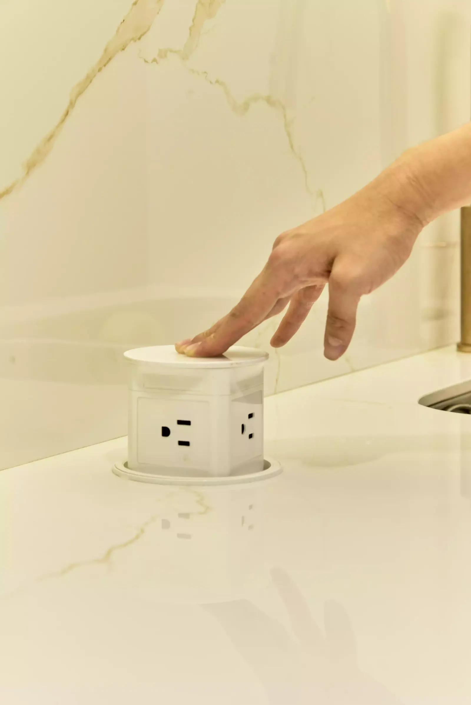 Mano presionando una toma eléctrica redonda integrada en el mesón claro de una cocina