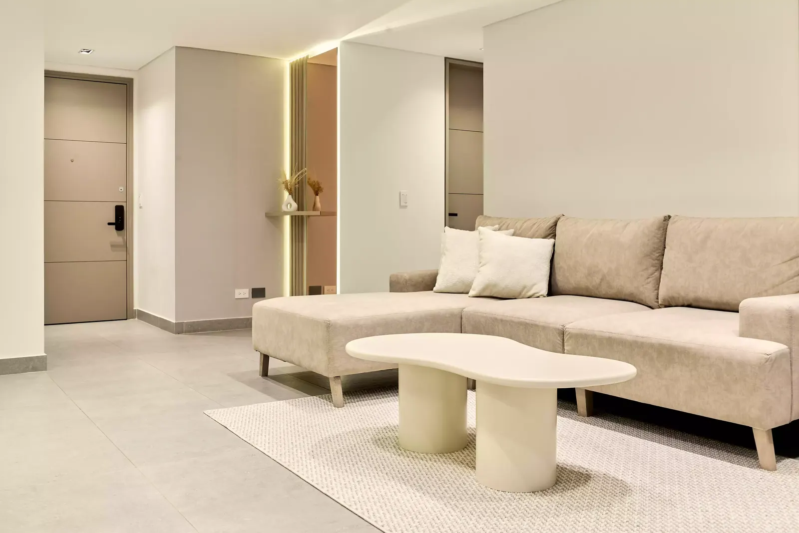 Sala y entrada de un apartamento remodelado, con muros claros y luz lineal en el cielo raso