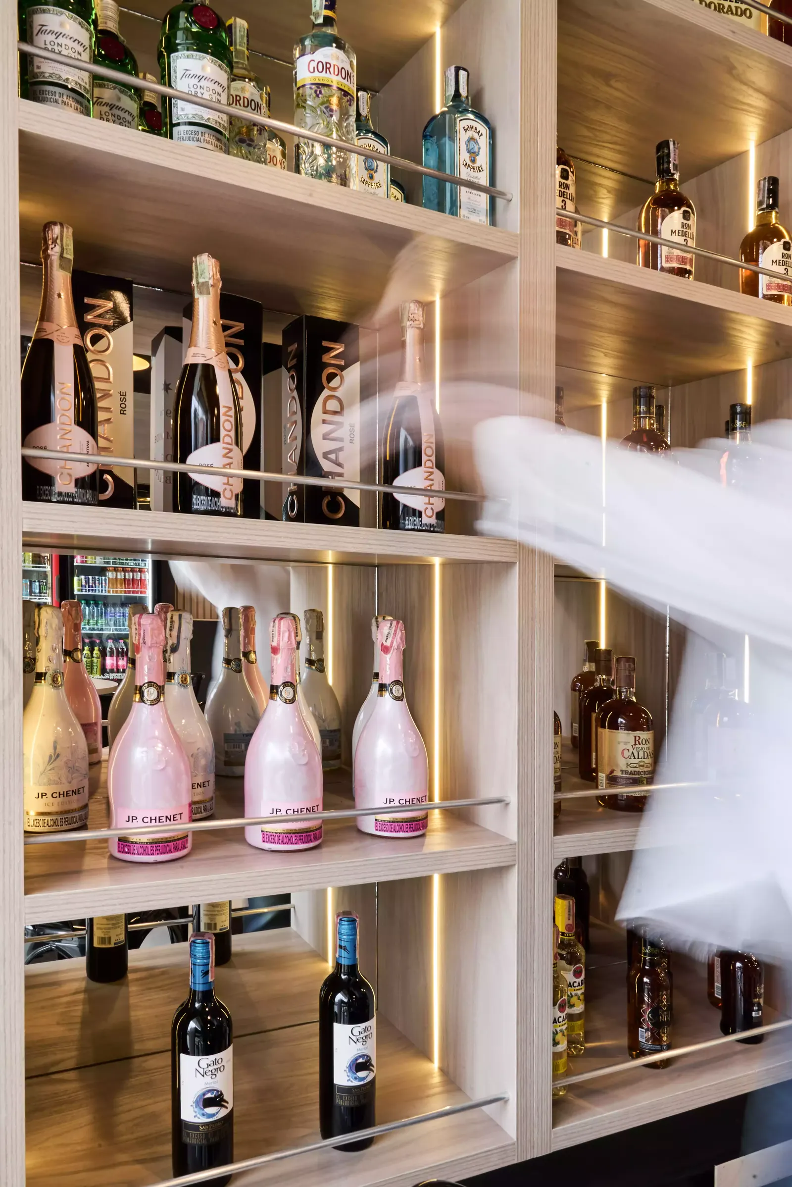 Estantería de madera clara con botellas de licor iluminadas por luz en cada nivel