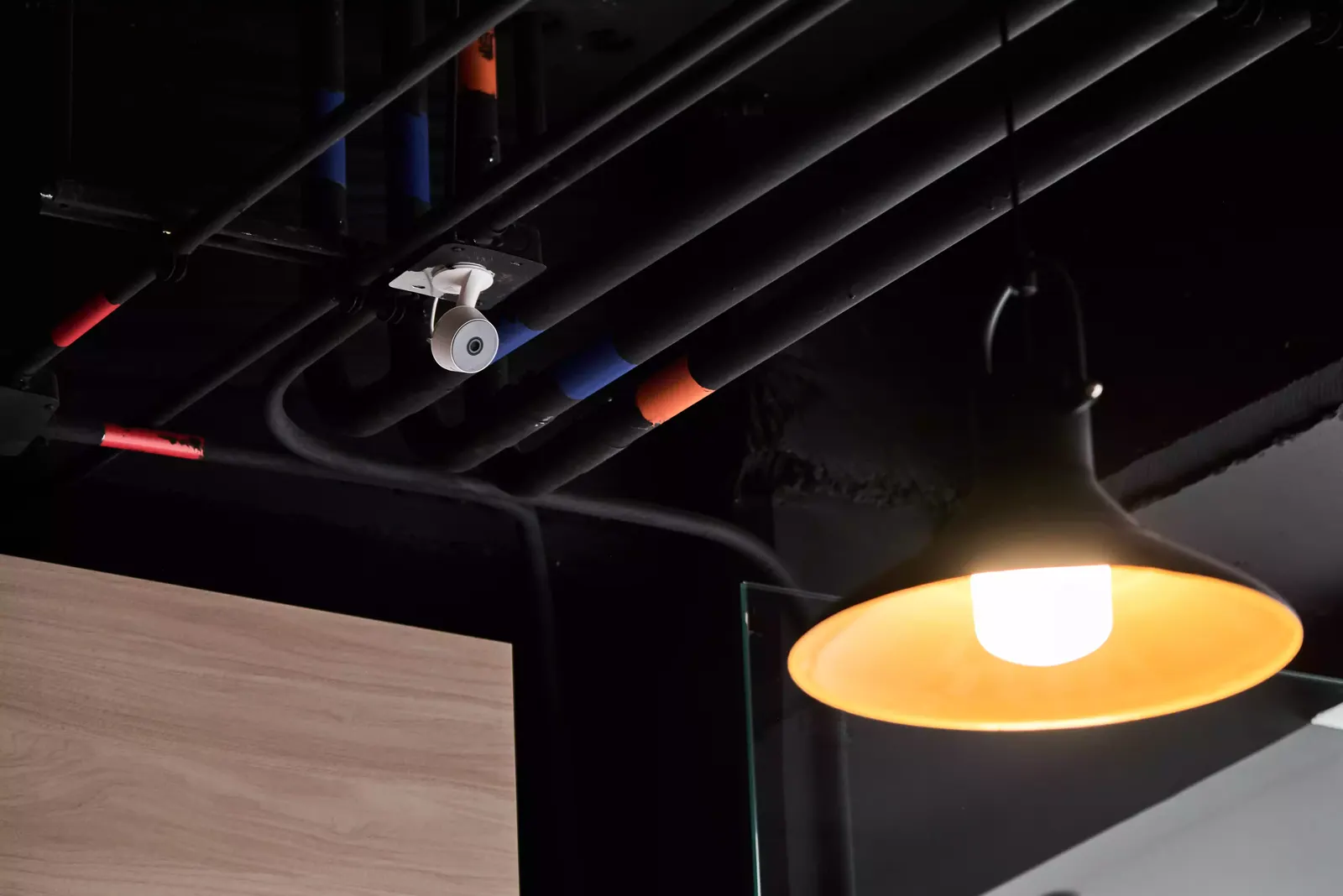 Lámpara colgante de luz cálida bajo un techo oscuro con ductos a la vista junto a un mueble de madera clara