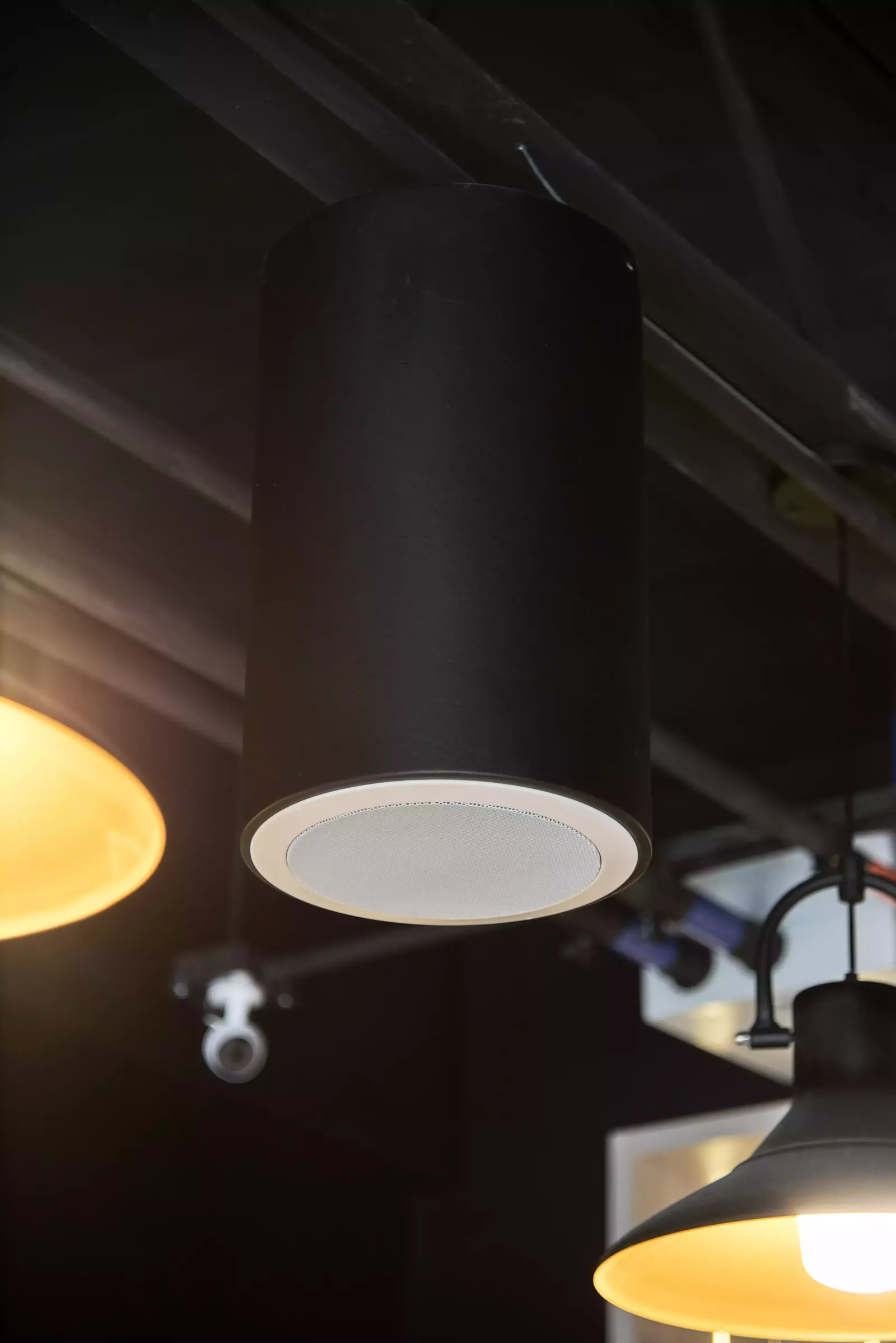 Parlante empotrado en el techo junto a lámparas colgantes negras de luz cálida