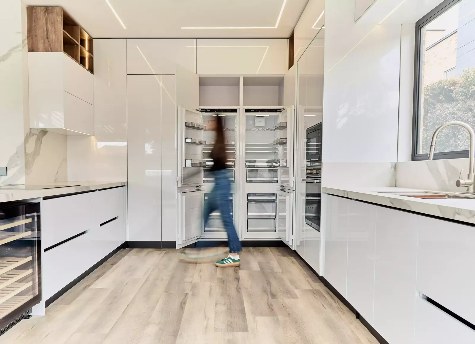 Cocina blanca con columnas de refrigeración empotradas, vinoteca y mesón en una casa