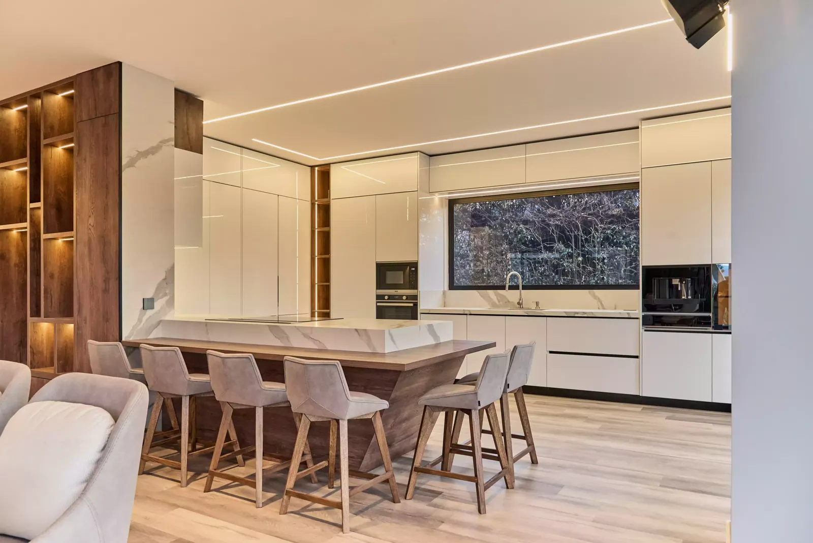 Cocina blanca de alto brillo con isla, barra con taburetes y nichos de madera iluminados