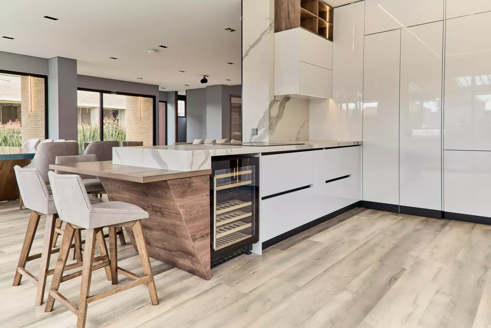 Cocina blanca con isla de madera, vinoteca y taburetes, en el proyecto Leo & Diana