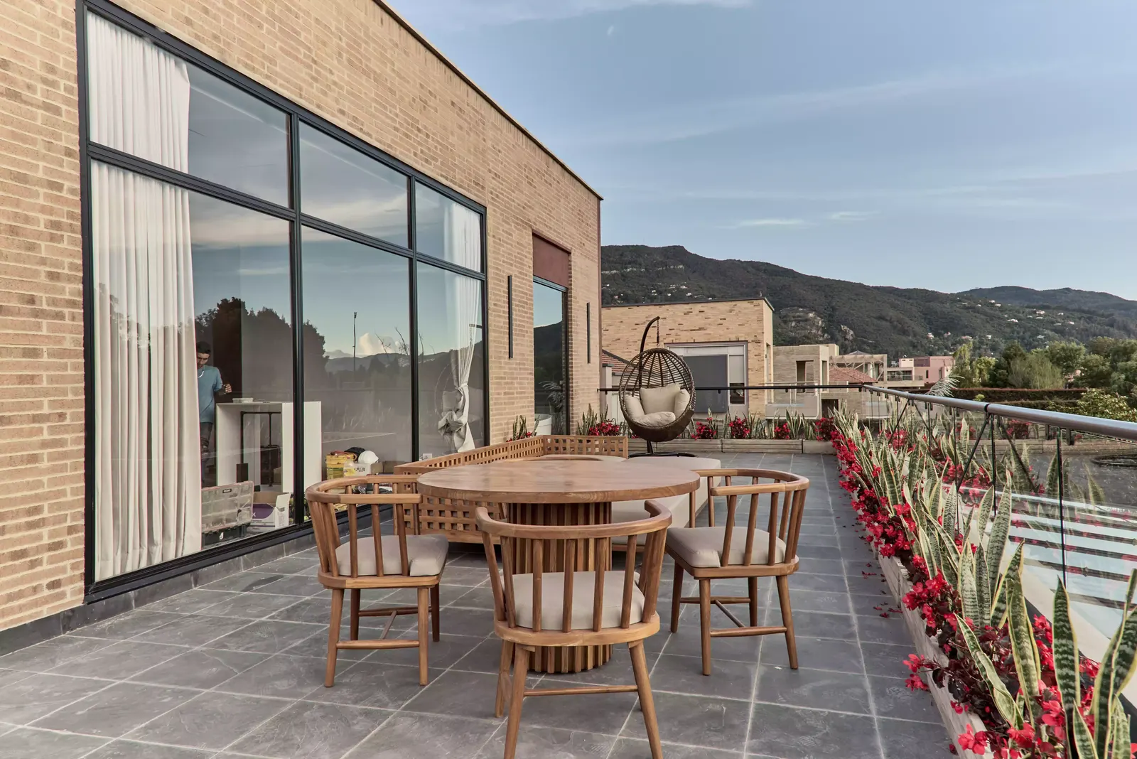 Terraza de una casa con grandes ventanales, piso de piedra y comedor exterior de madera