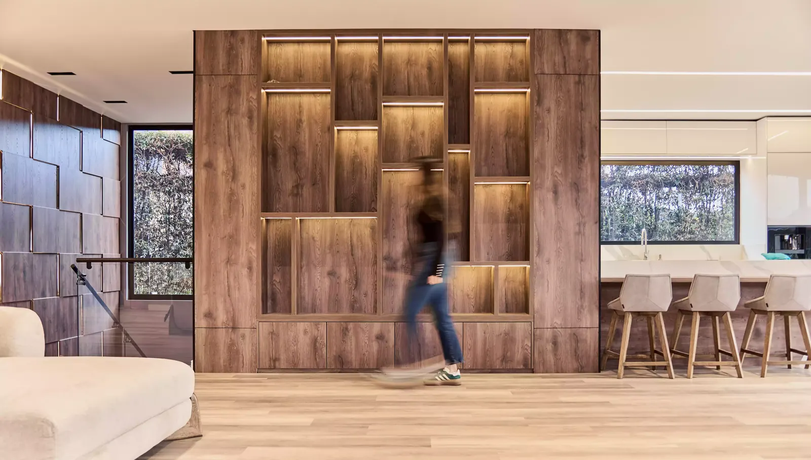 Mueble de madera a medida con nichos e iluminación lineal integrada, junto a la cocina y la escalera de una casa