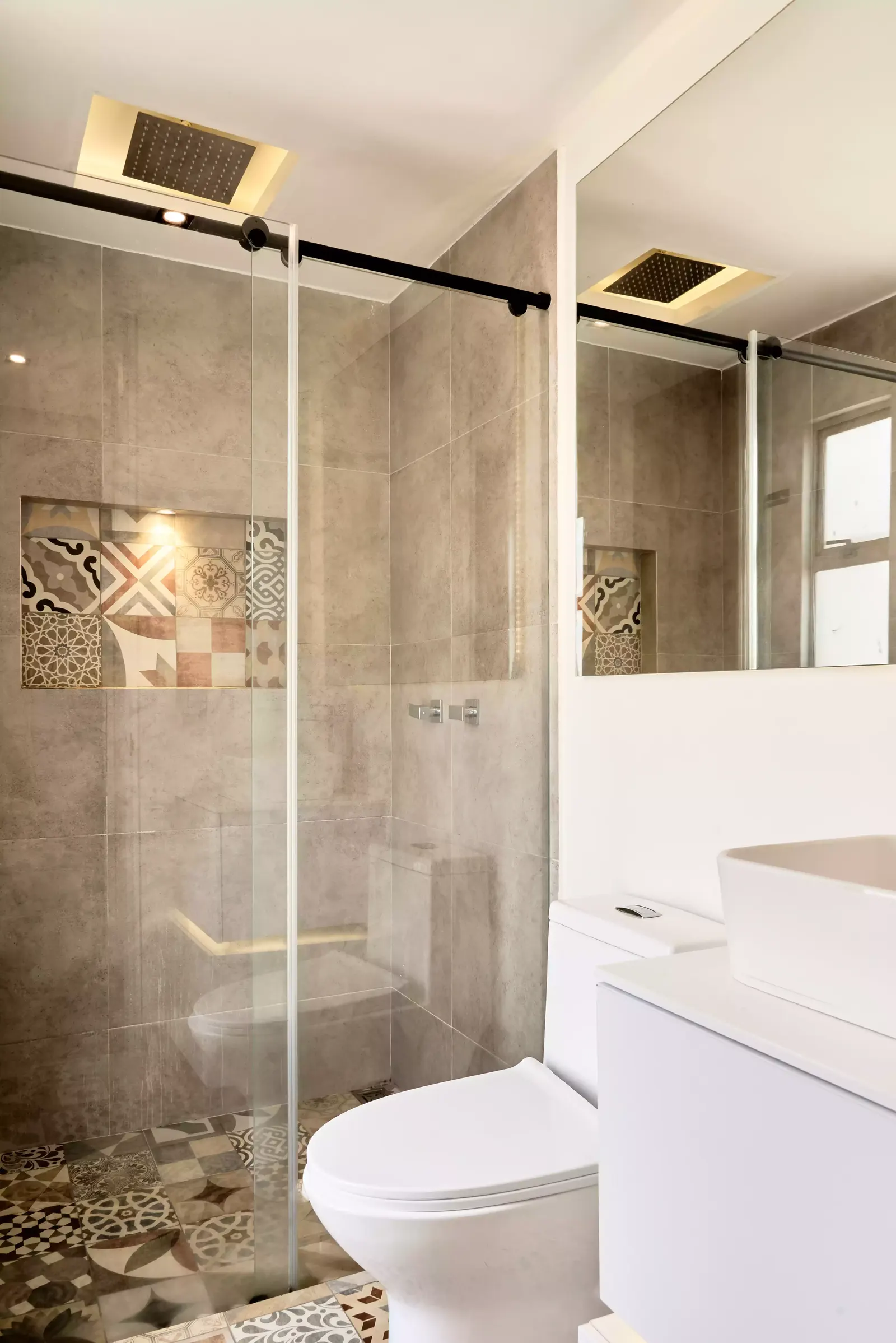 Ducha en vidrio con nicho de baldosa decorada y revestimiento gris en un baño de apartamento