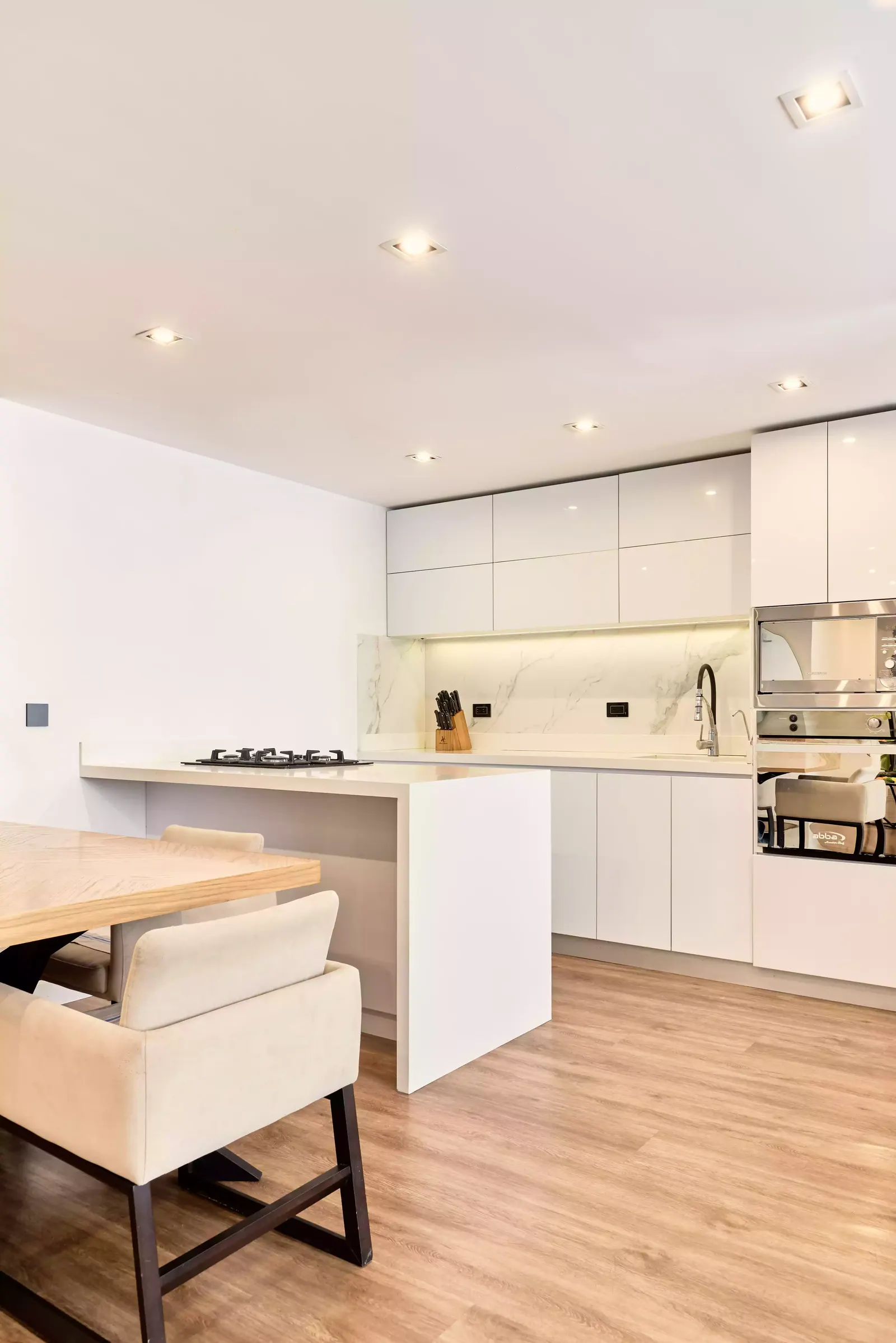 Cocina blanca con isla y mesa de comedor de madera en primer plano en un apartamento