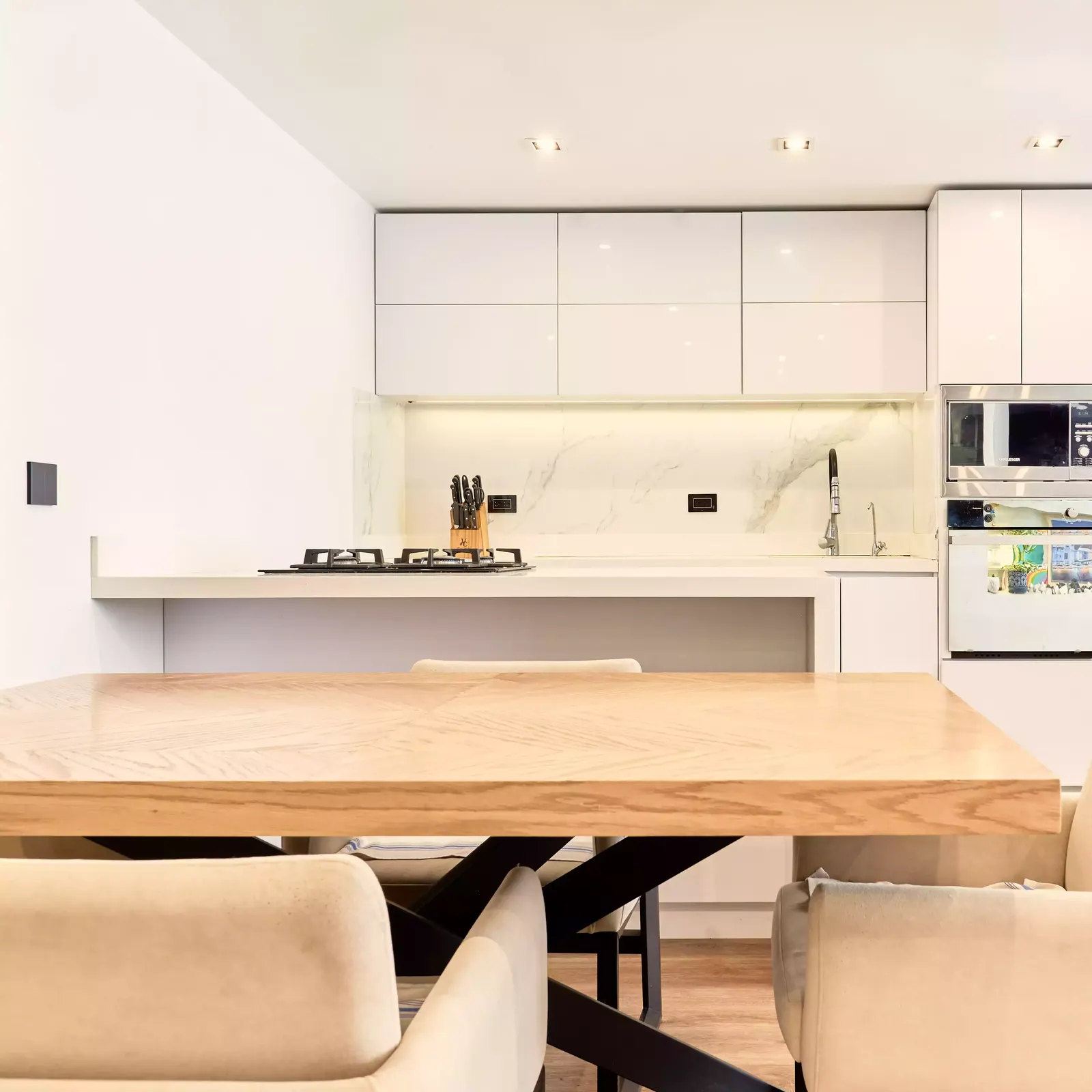 Cocina blanca con isla y mesa de comedor de madera en primer plano en un apartamento