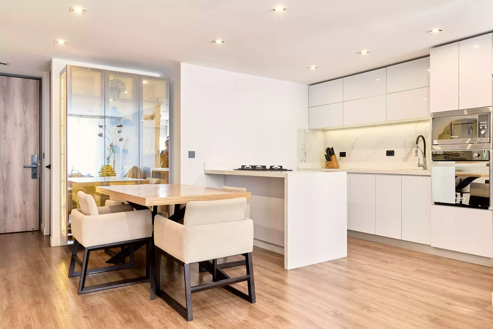 Cocina blanca con isla y comedor de madera con vitrina iluminada en un apartamento remodelado en Cedritos