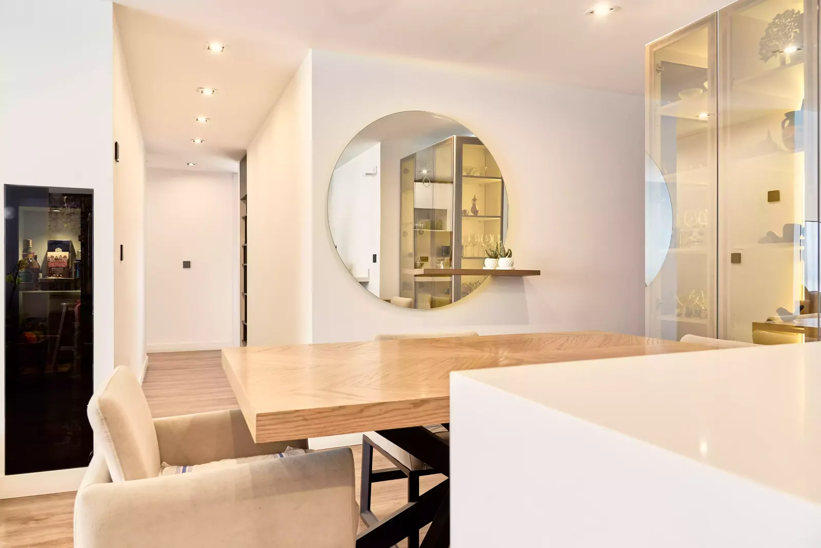 Comedor con mesa de madera, vitrina iluminada y piso de madera en un apartamento con acabados completos