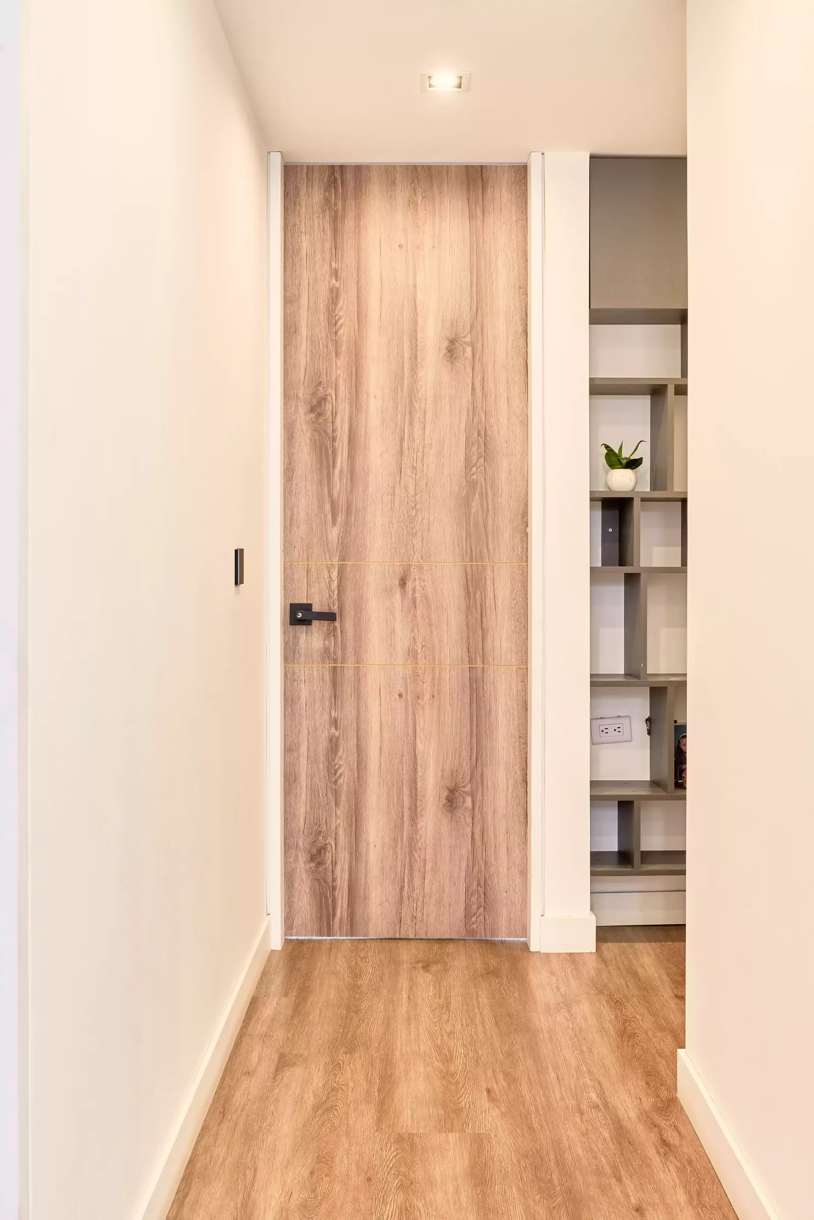 Pasillo con una puerta de madera de piso a techo y estantes a la vista al fondo
