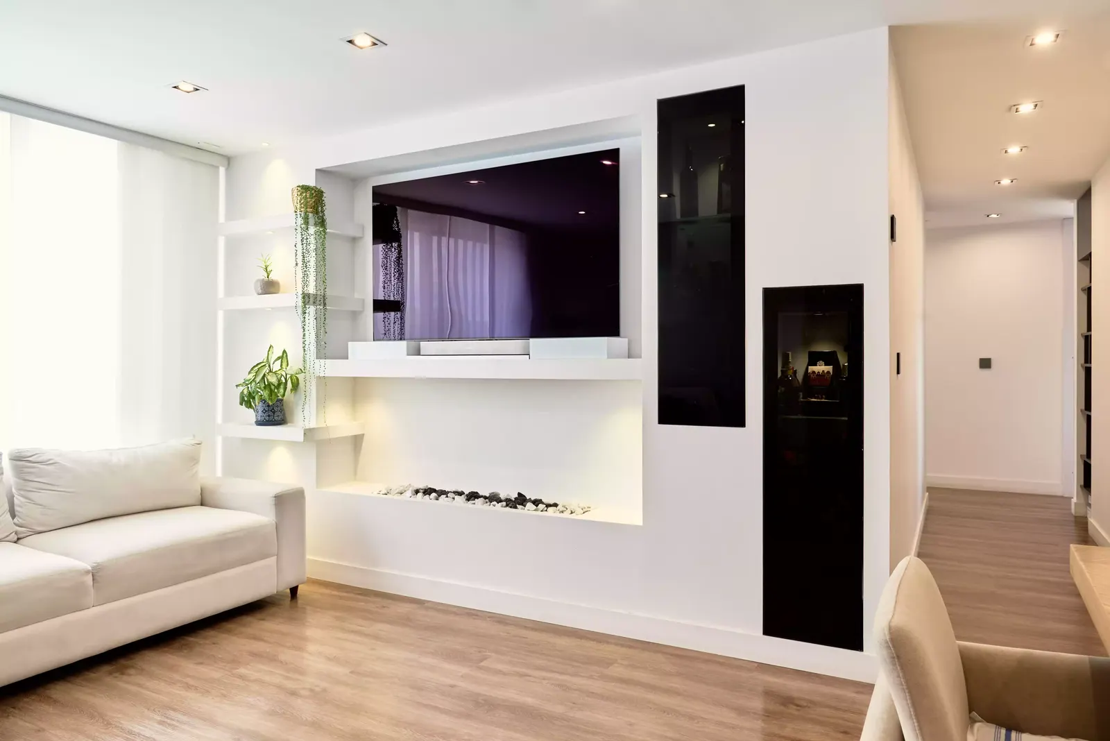 Sala de apartamento con muro de televisión blanco, chimenea lineal, repisas y vitrinas con vidrio negro