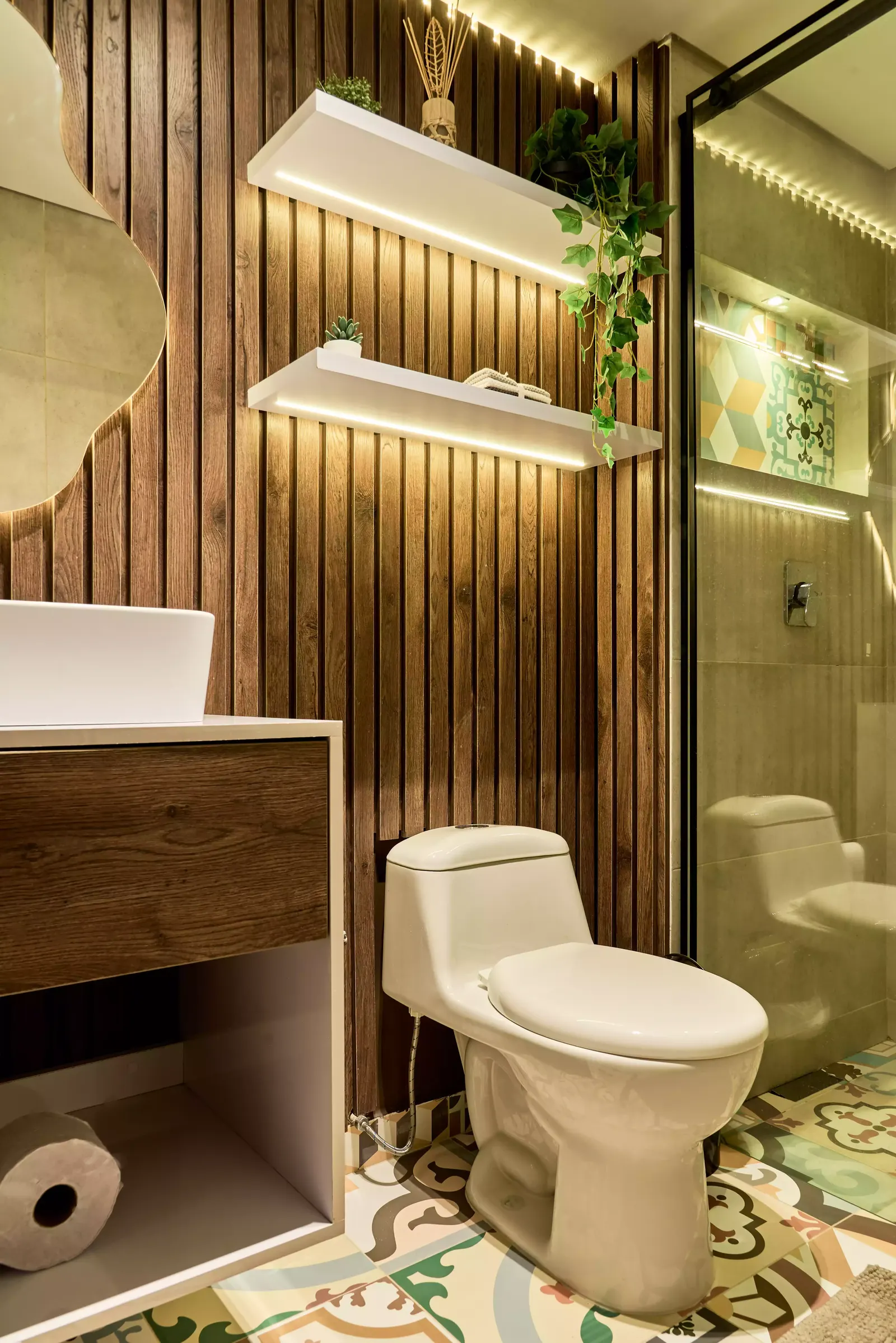 Baño con muro de listones de madera, repisas flotantes iluminadas, mueble de lavamanos y piso de baldosa decorada