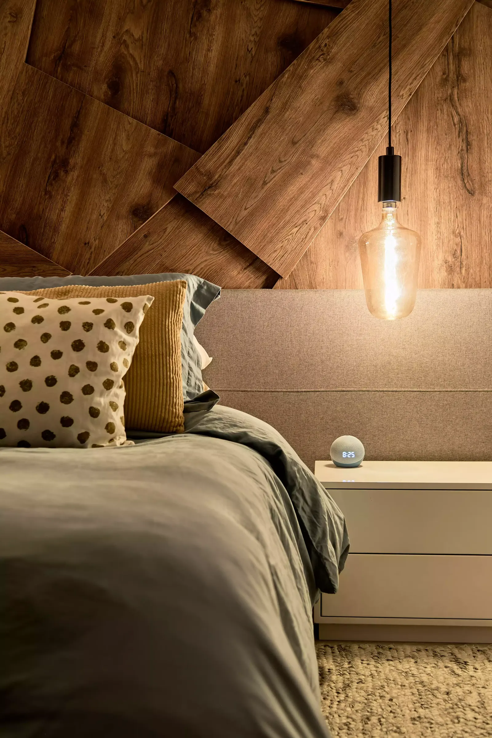 Detalle del cabecero de madera con una lámpara colgante de filamento junto a la cama