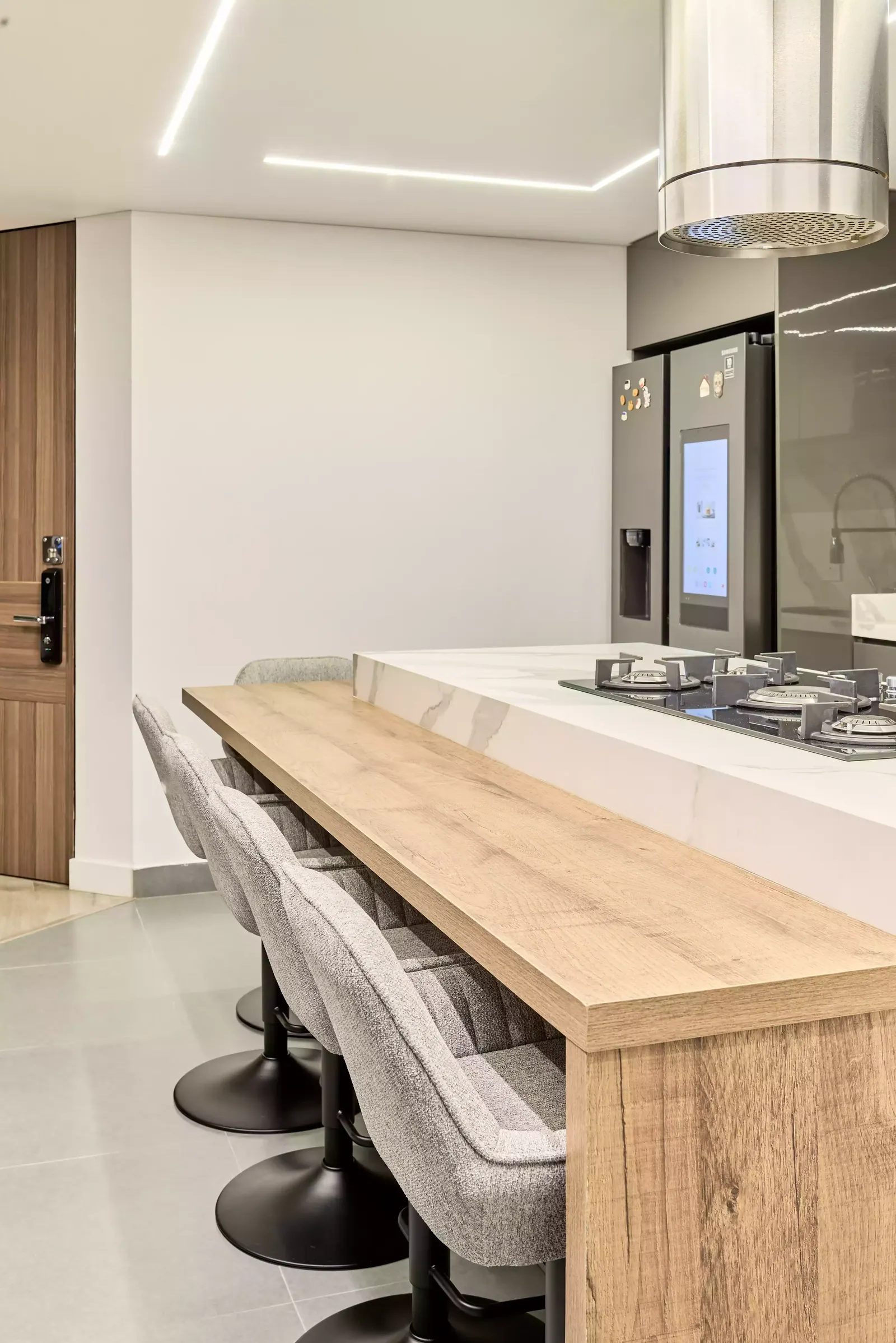 Cocina con barra de desayuno en madera y taburetes junto a una isla clara