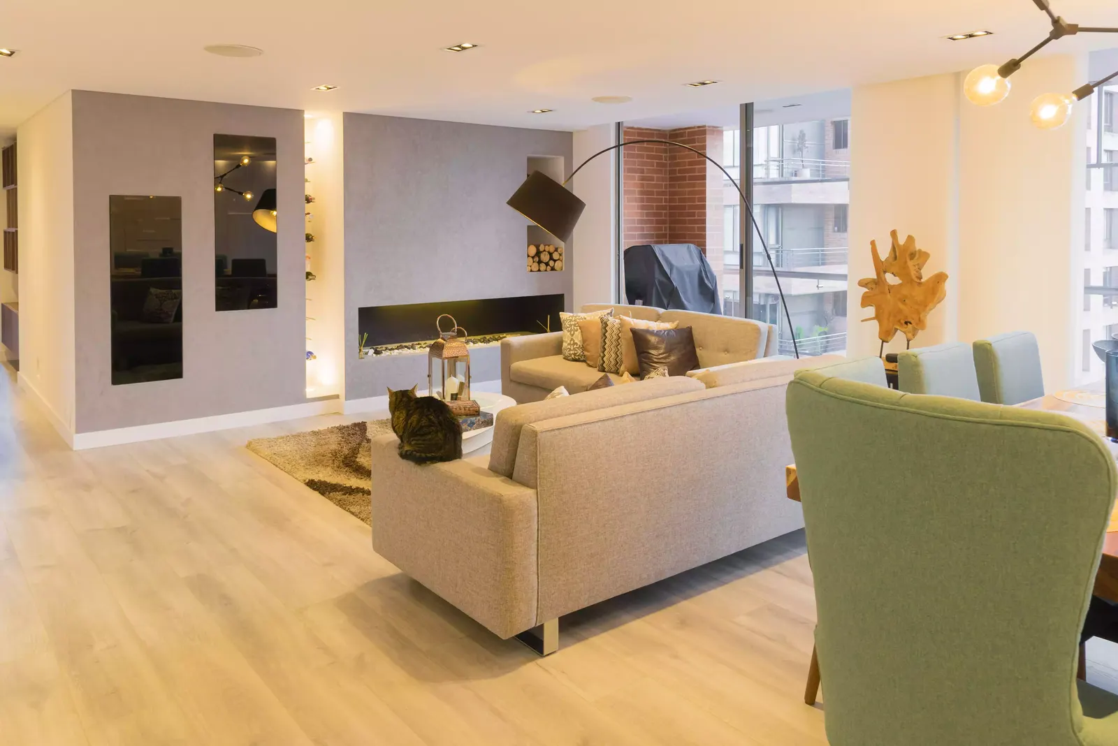 Sala abierta de apartamento con chimenea lineal, sofás de tonos cálidos y luz indirecta