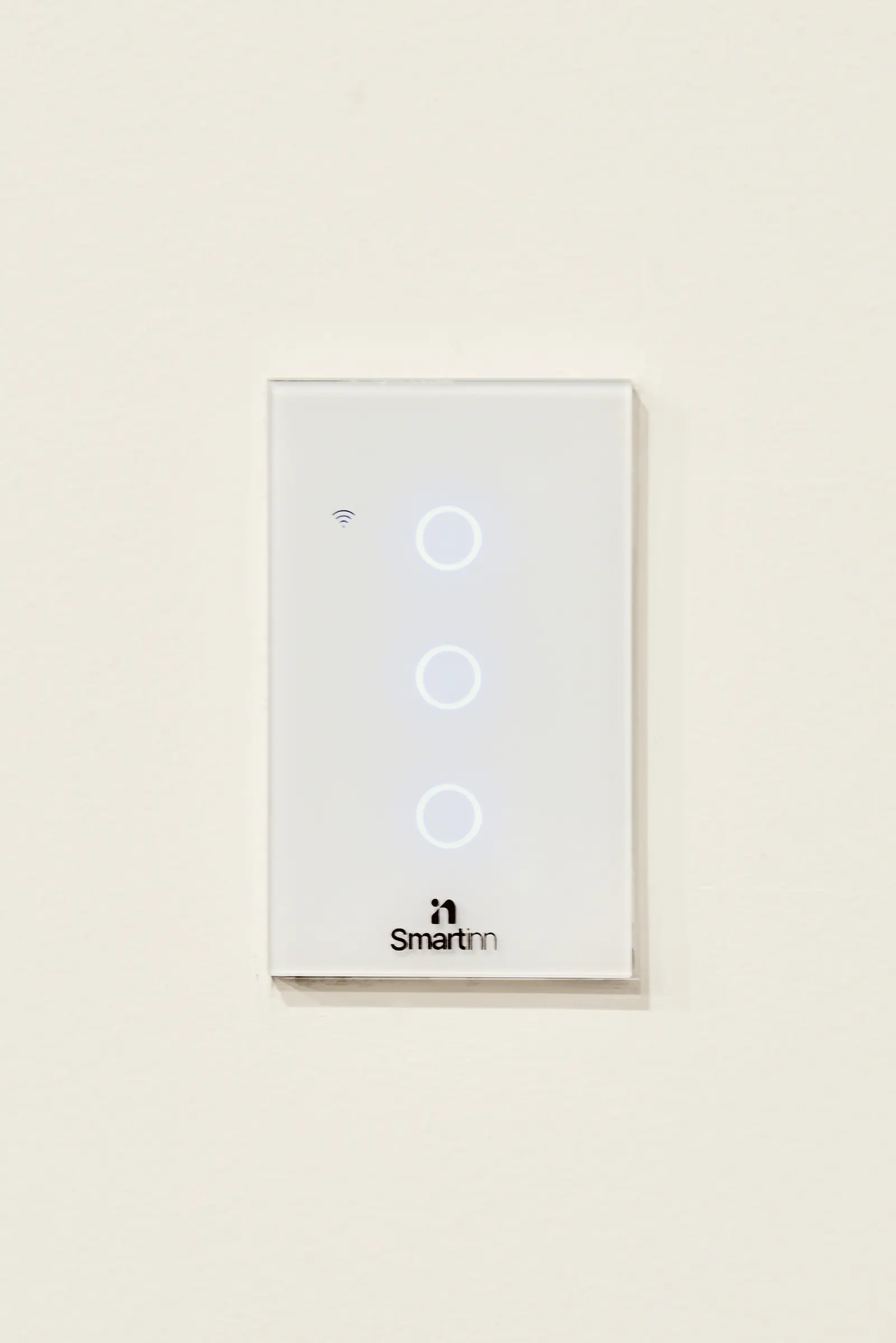 Interruptor táctil de tres botones blanco con el logo de Smartinn sobre un muro claro